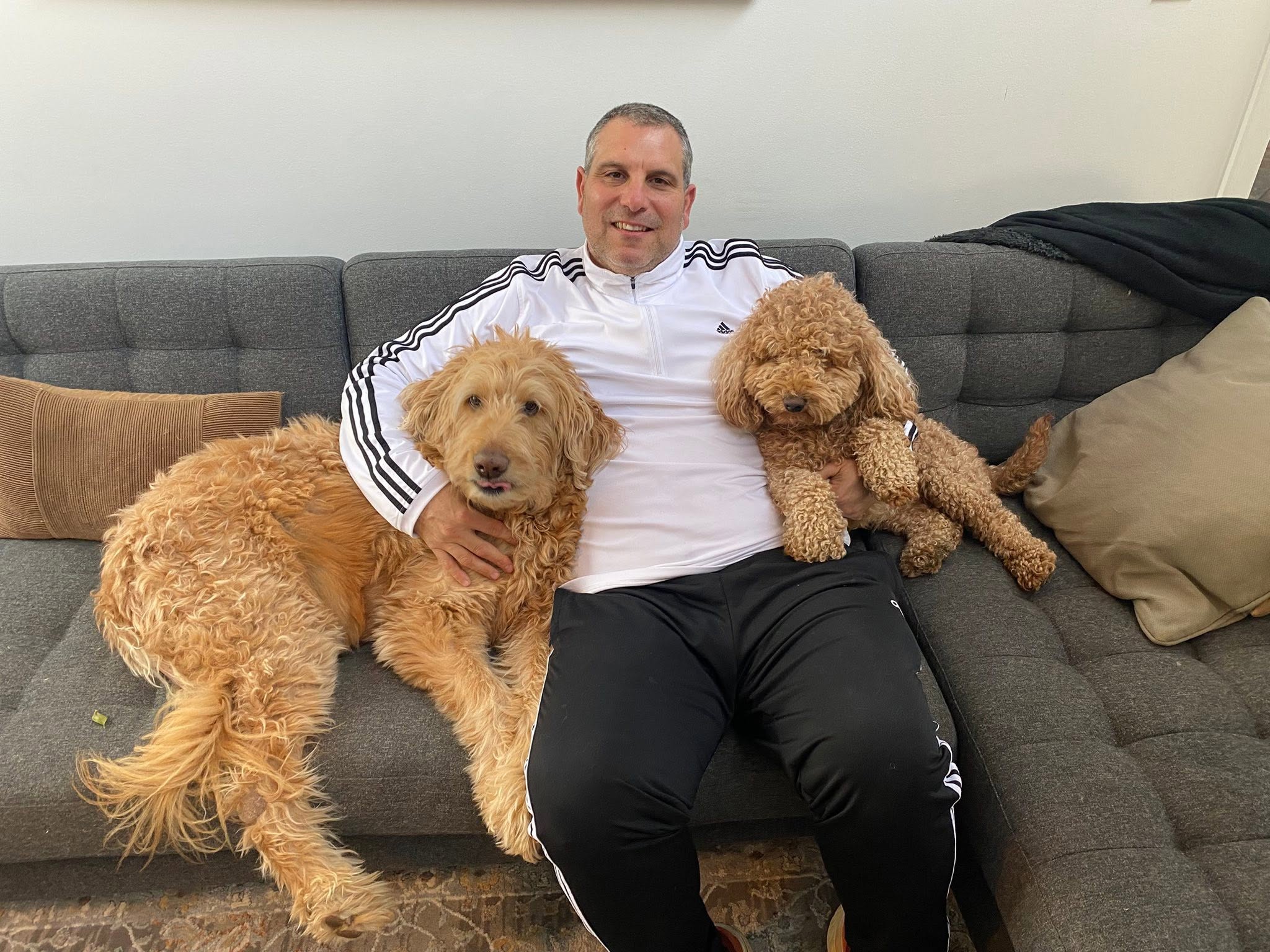 A man relaxing on a couch with his two golden doodles lounging beside him